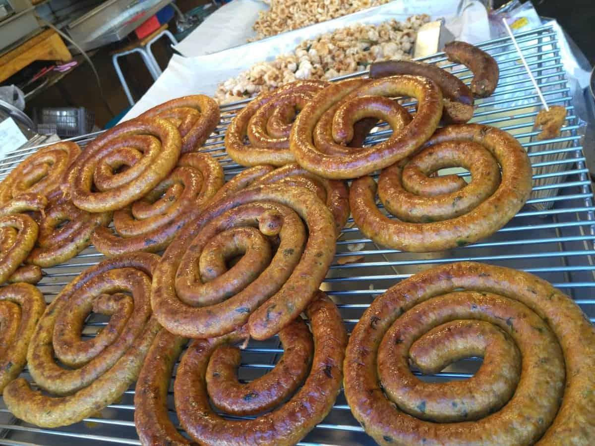 Northern Thai sausage (Sai Ua) coils on a grill in a market in Chiang Mai, Thailand.