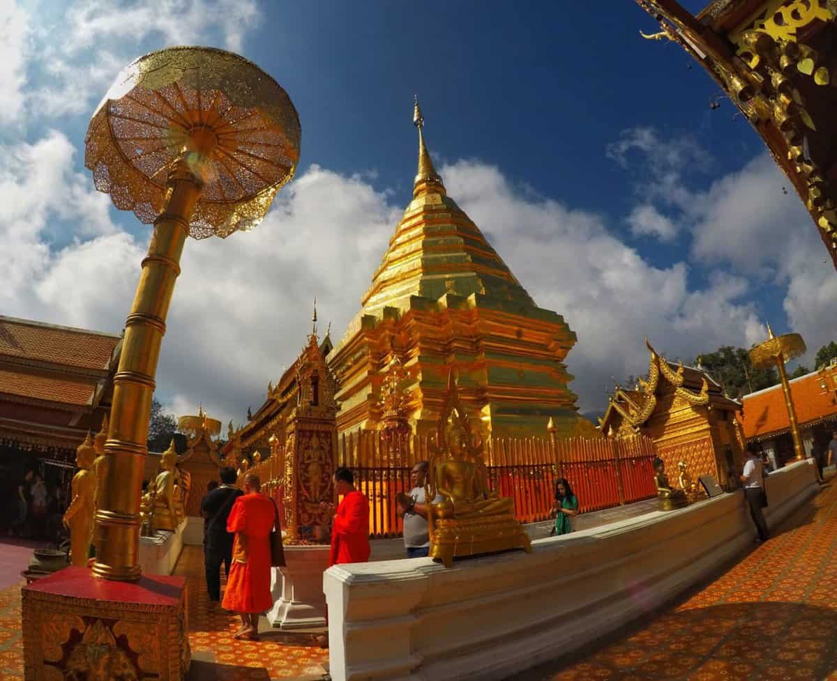 Golden stupa and devotees at Wat Phra That Doi Suthep in Chiang Mai, Thailand, under a blue sky.